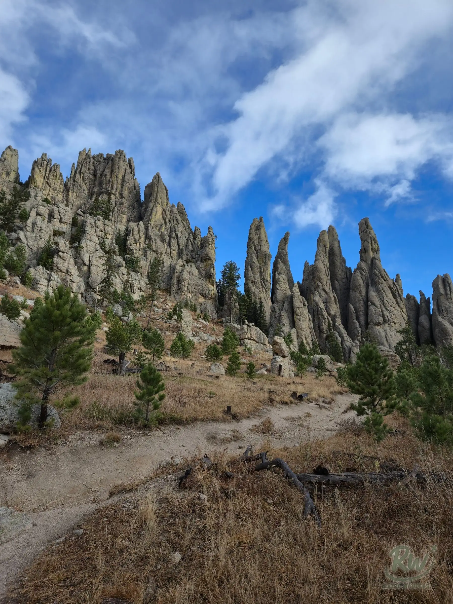A dirt trail climbing a grassy slope toward two clusters of granite spires