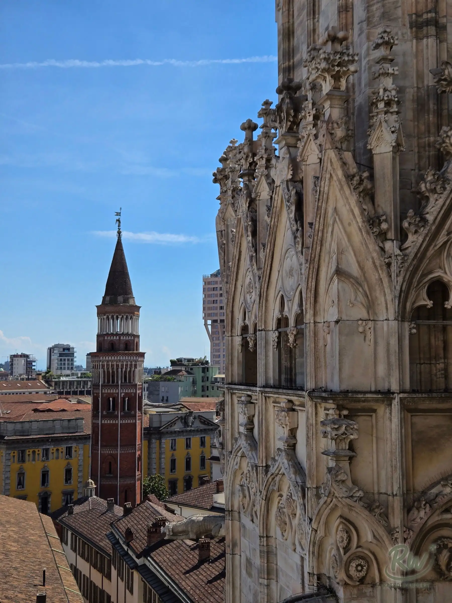 Carved Gothic stonework on the side of the Duomo, a brick bell tower and rooftops behind