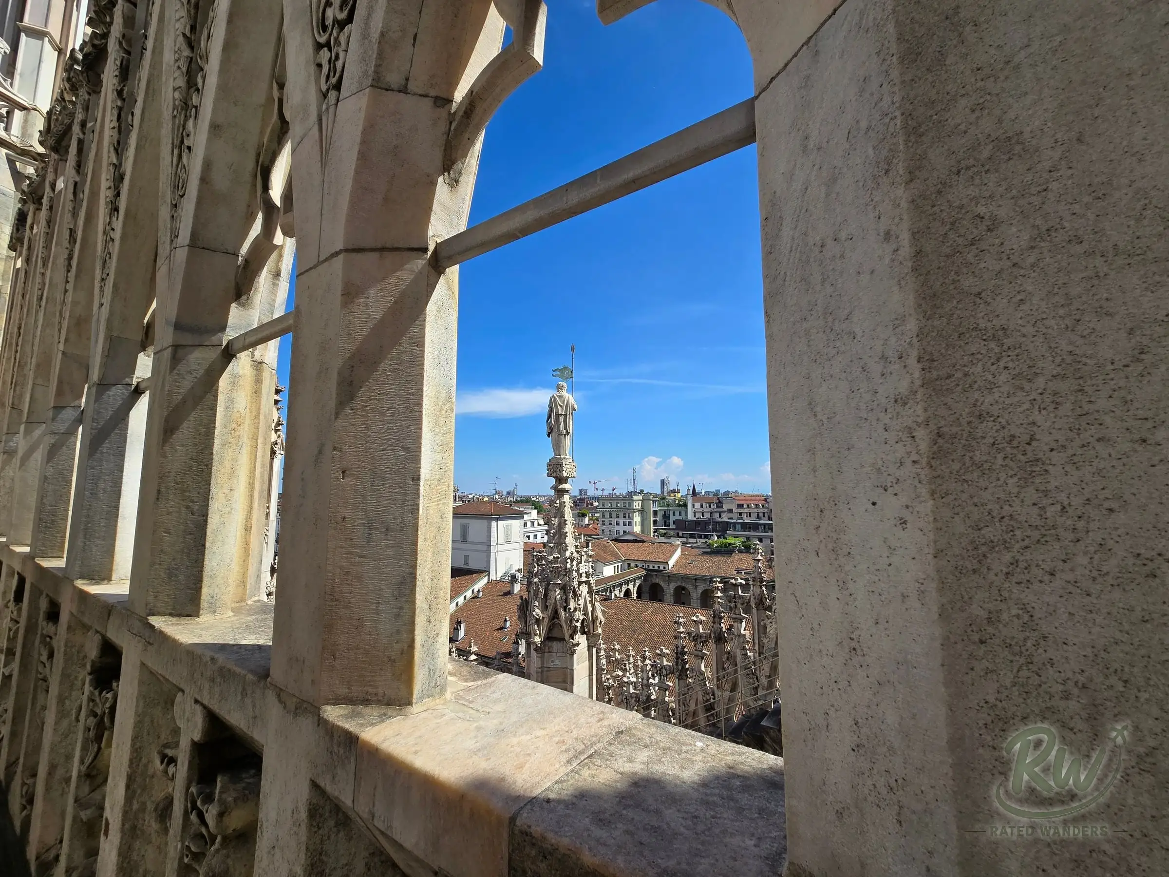 A spire and city rooftops framed through the stone arches of the Duomo terrace