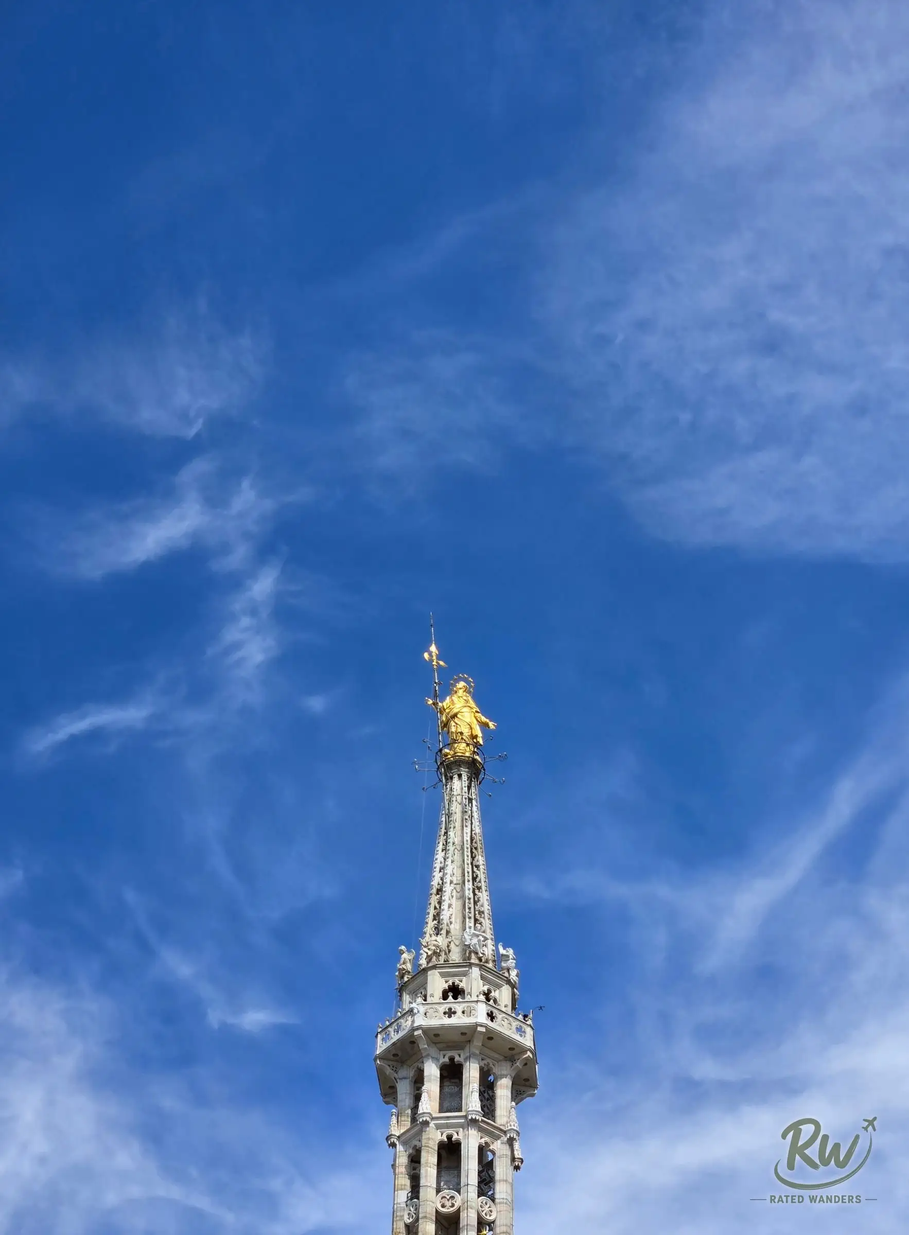 The golden Madonnina statue on top of the Duomo’s highest spire against a blue sky