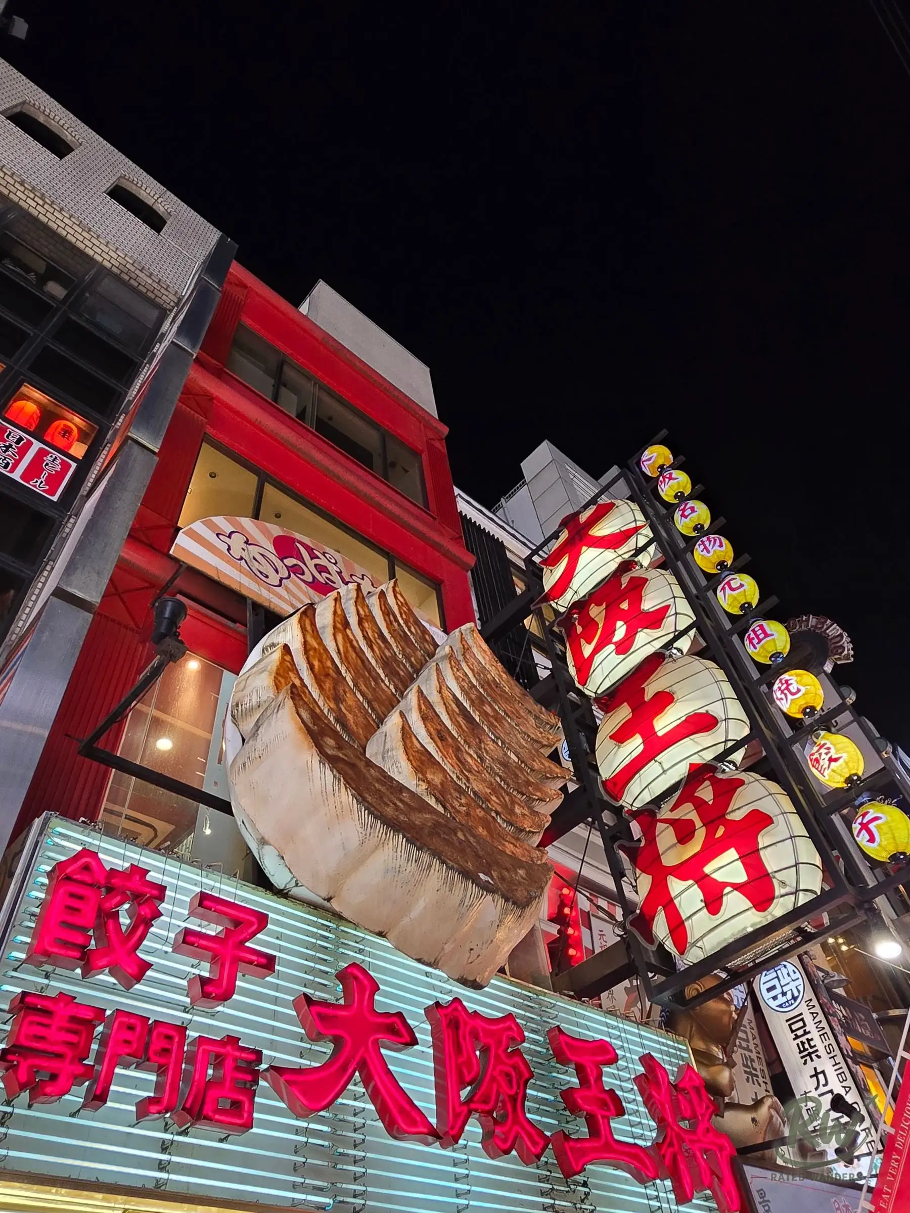 A giant gyoza dumpling sign and red paper lanterns on a restaurant front at night