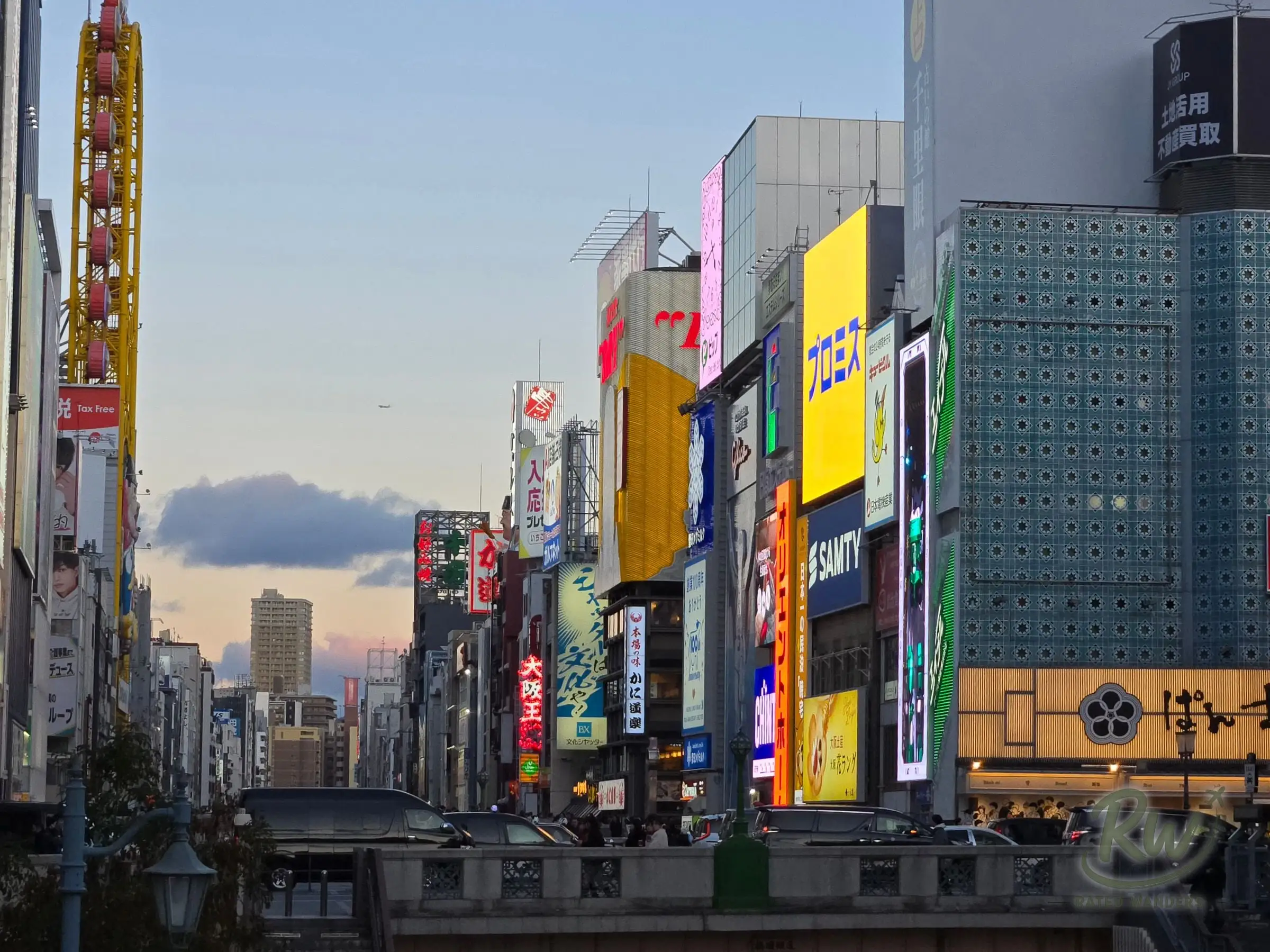 Tall billboards and signs lining the Dotonbori canal under a pale evening sky