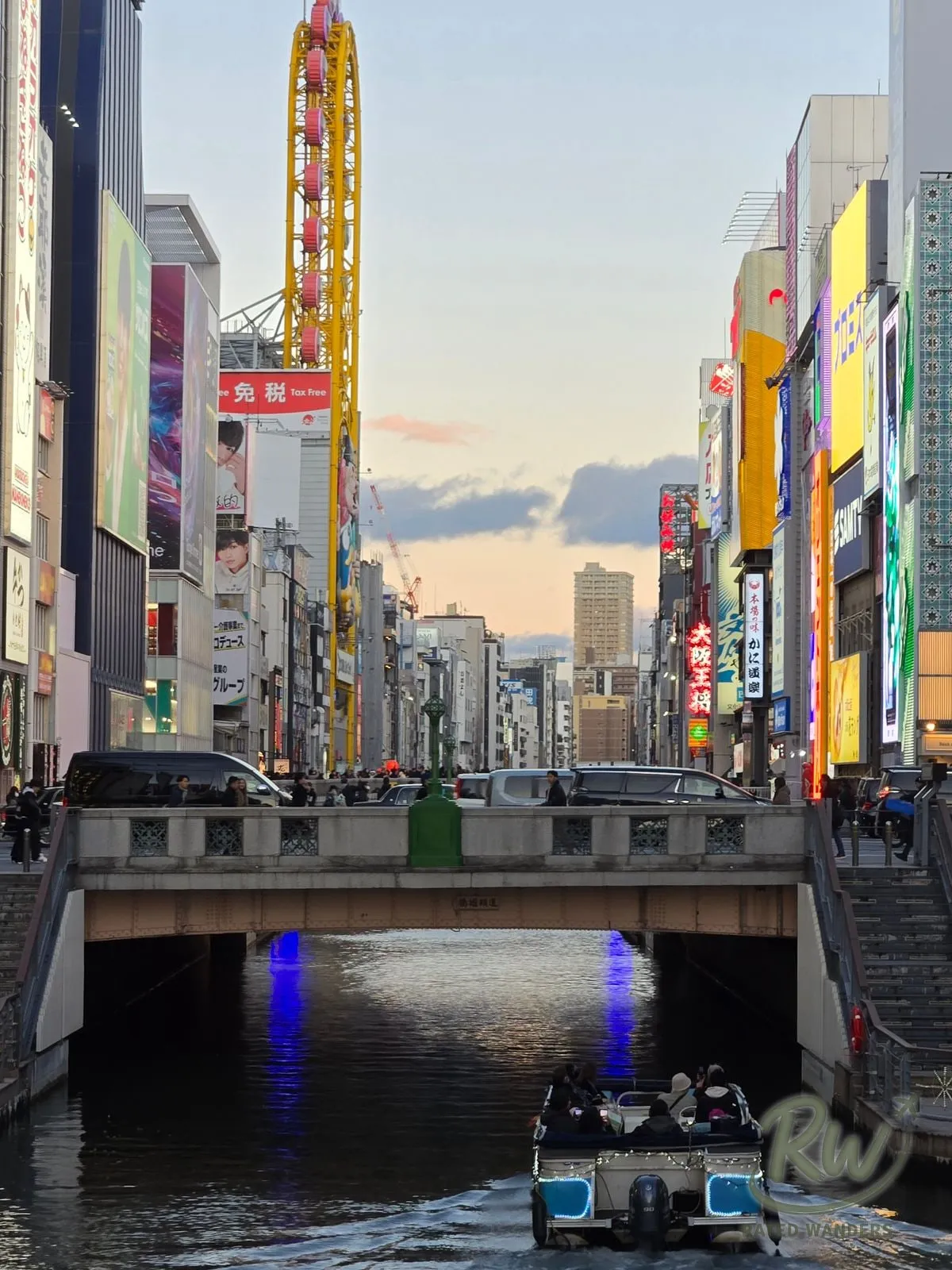 A cruise boat passing under a bridge on the Dotonbori canal at dusk