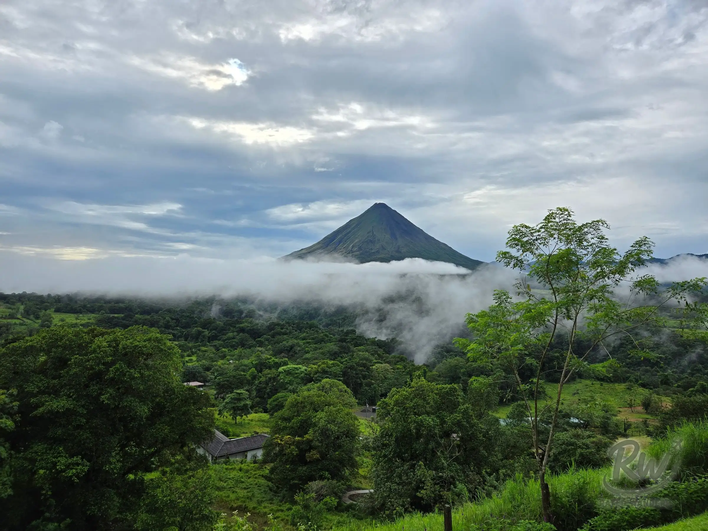 Arenal volcano rising above a low band of cloud, jungle and farmland filling the valley below
