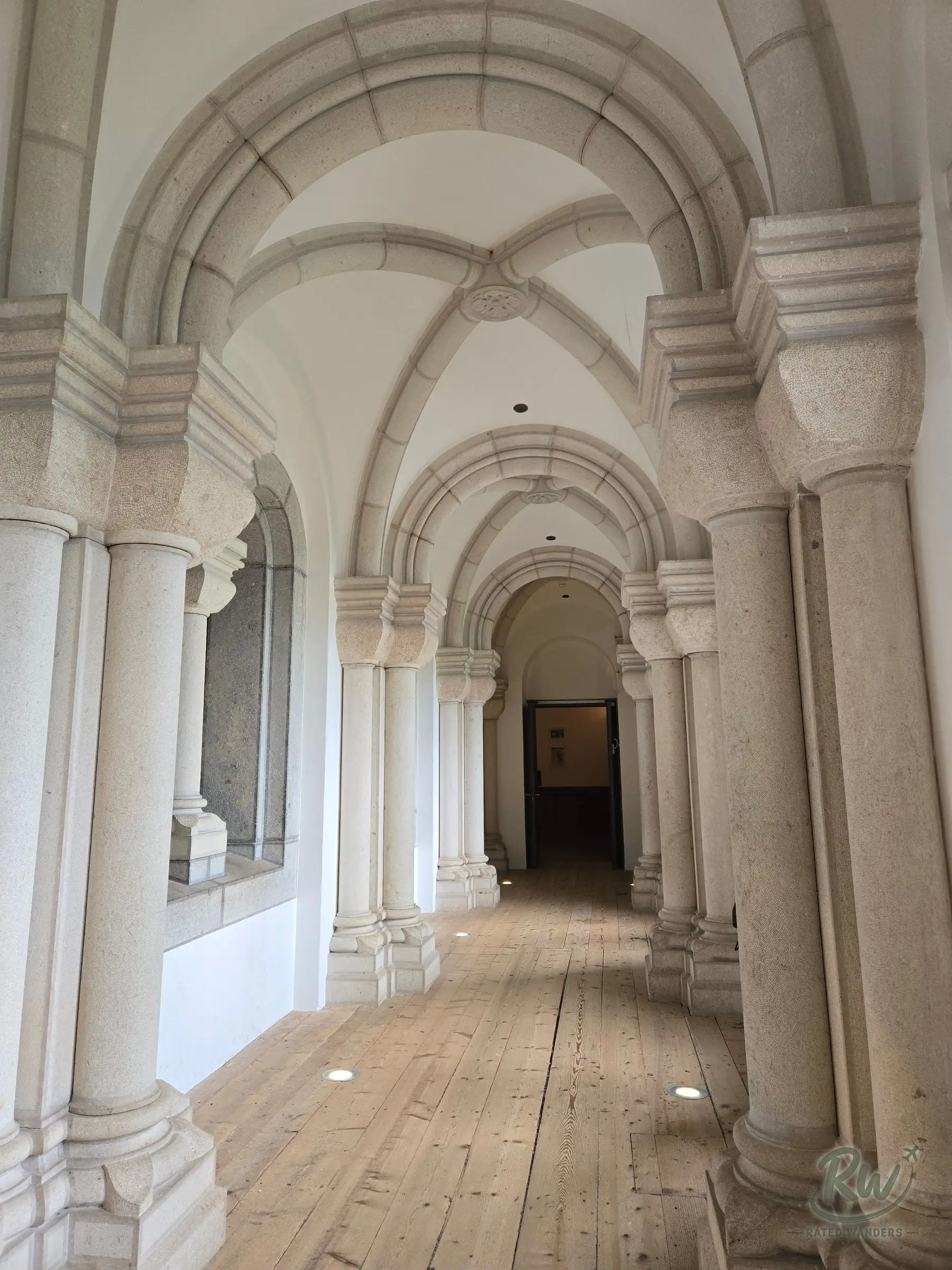 A vaulted stone corridor inside the castle, columns and arches over a plank floor
