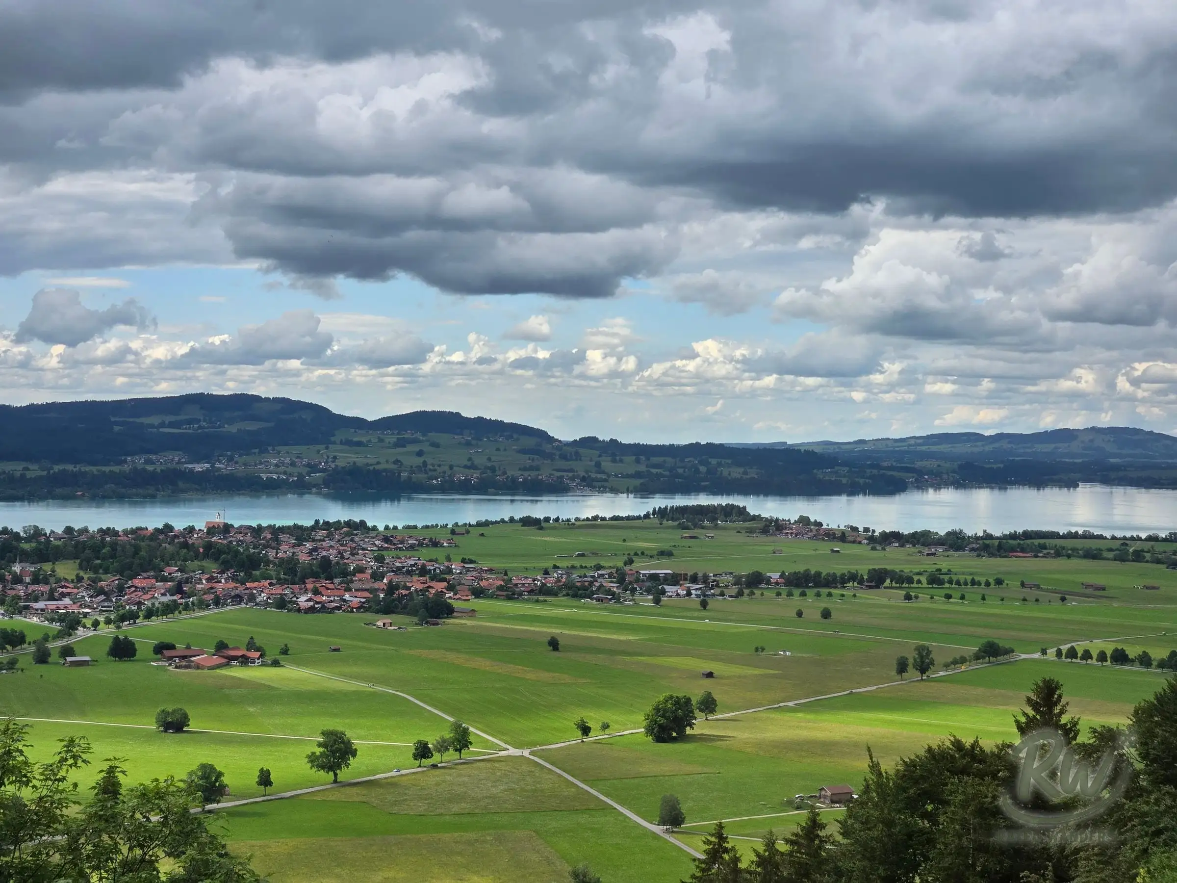 Farmland, a village and a lake spread across the Bavarian plain under broken cloud