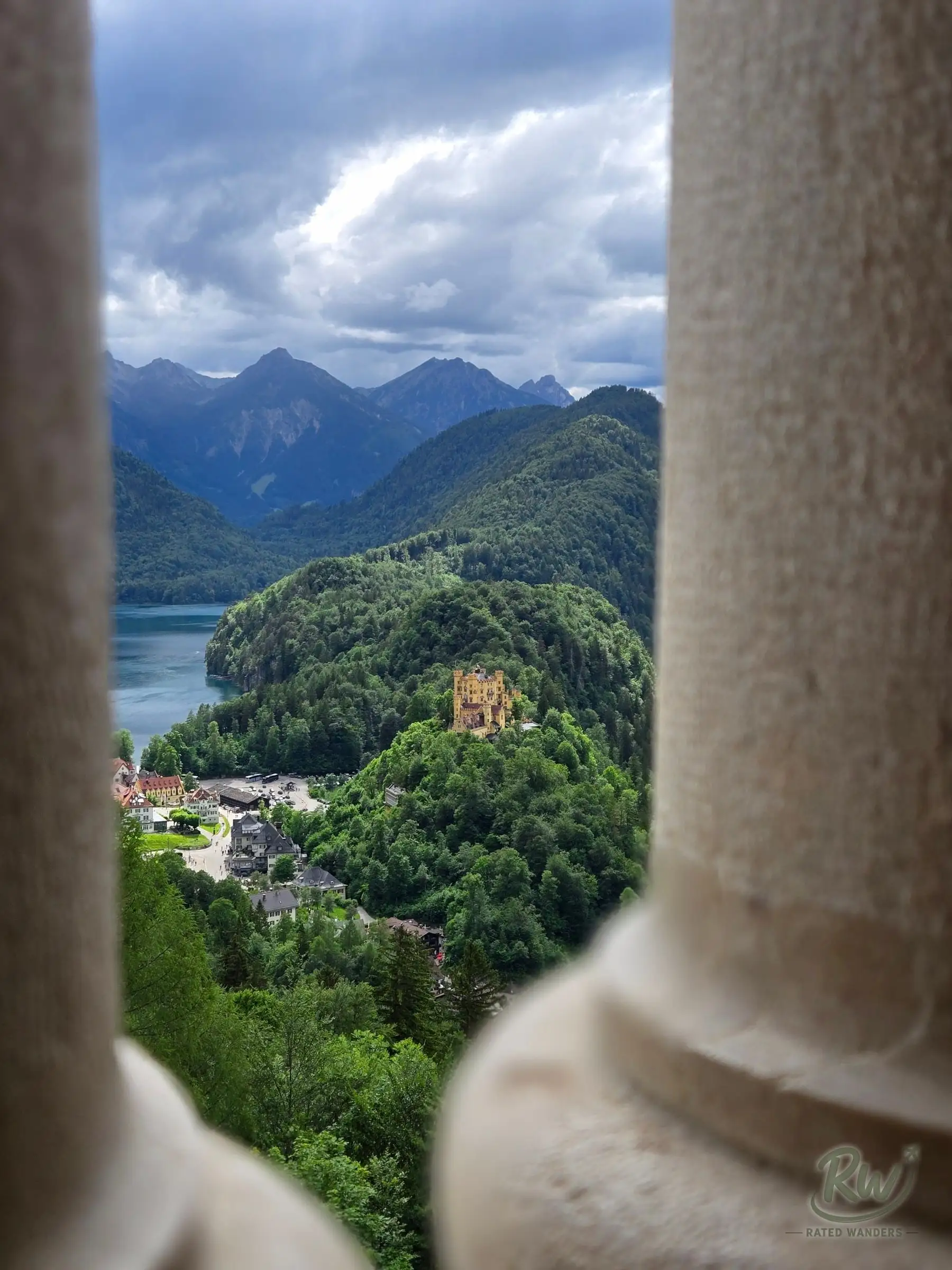 Hohenschwangau Castle on its wooded hill, framed between two stone columns of a castle balcony