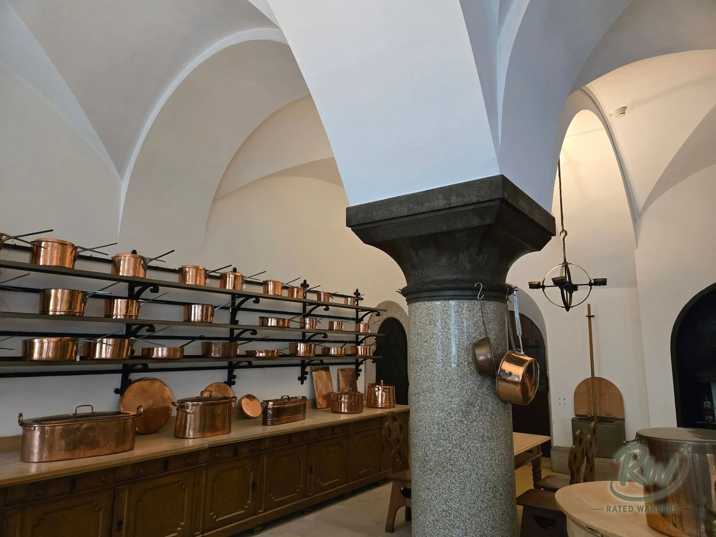 The castle kitchen, copper pots on iron racks under a vaulted ceiling