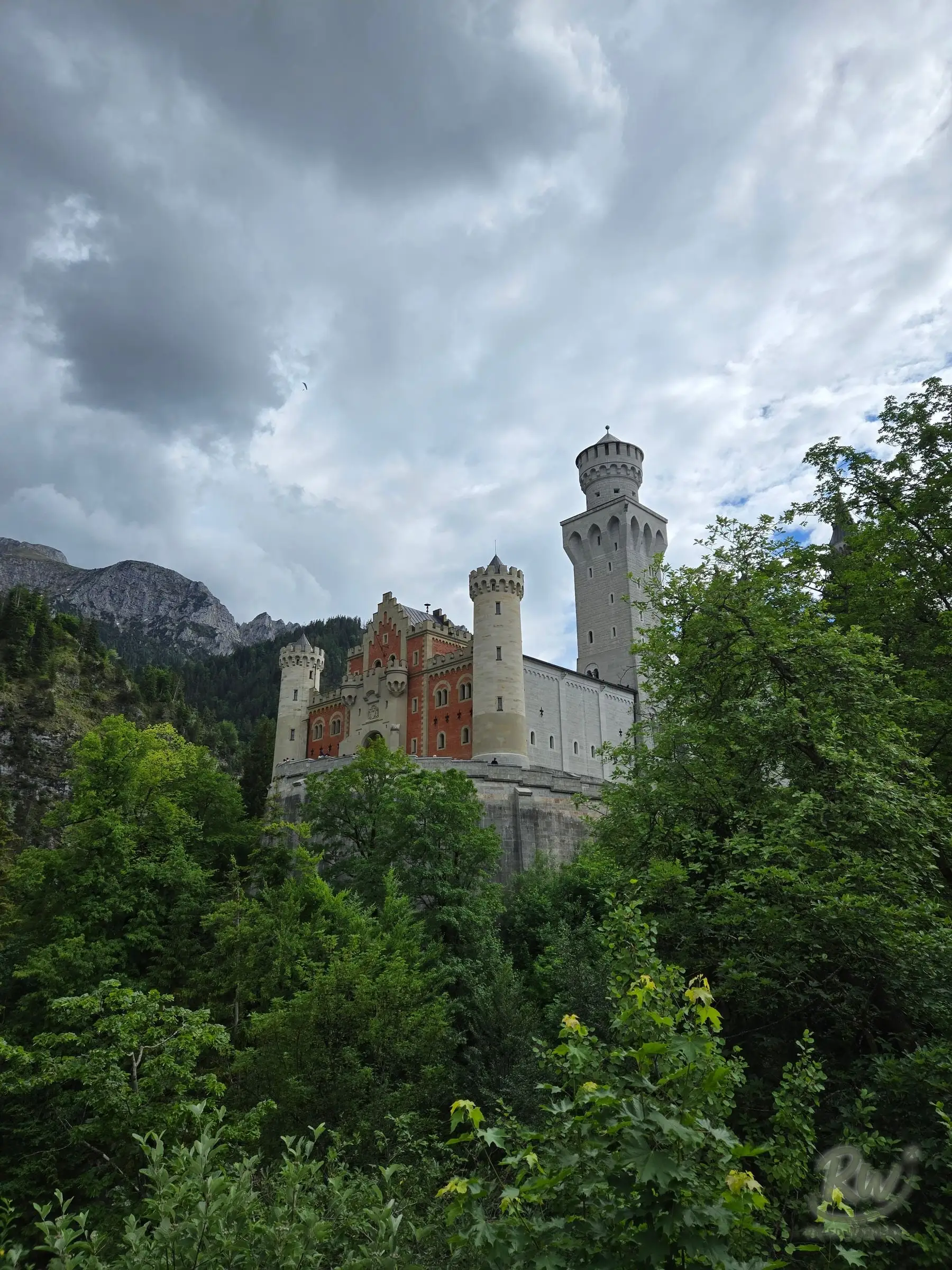 The red brick gatehouse and towers of Neuschwanstein Castle rising above the trees on the path up