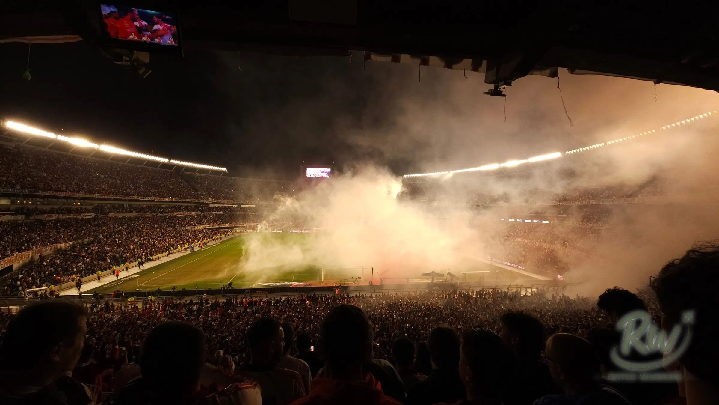 Thick smoke from flares drifting across the floodlit pitch above a packed home end