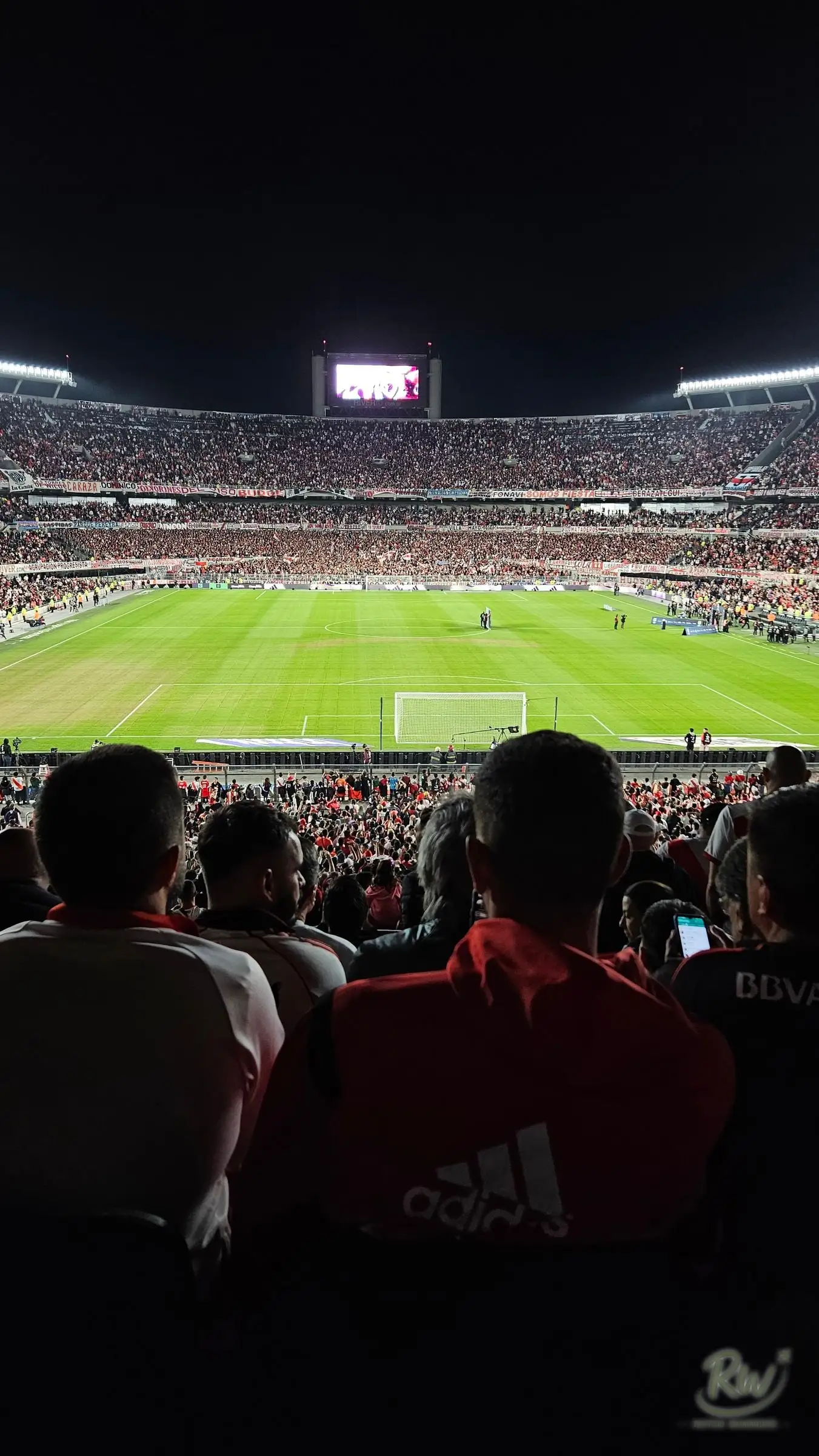 The view over supporters in red and white toward the floodlit pitch at night