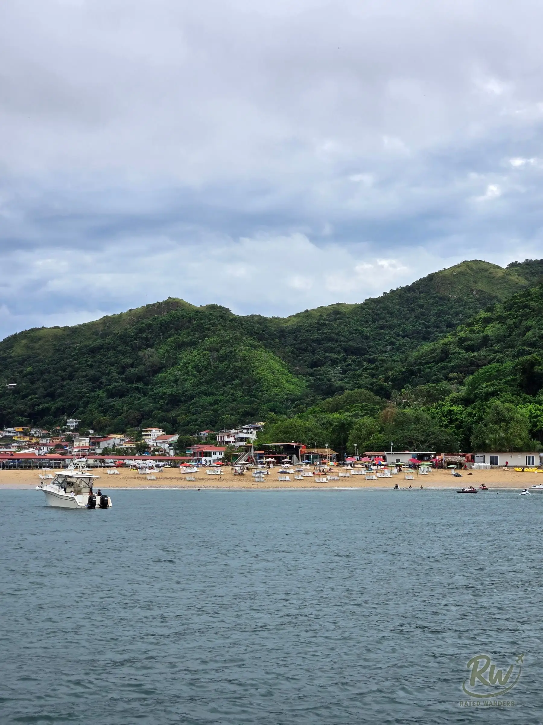 Rows of parasols and loungers along Playa Honda, a boat anchored offshore and green hills behind
