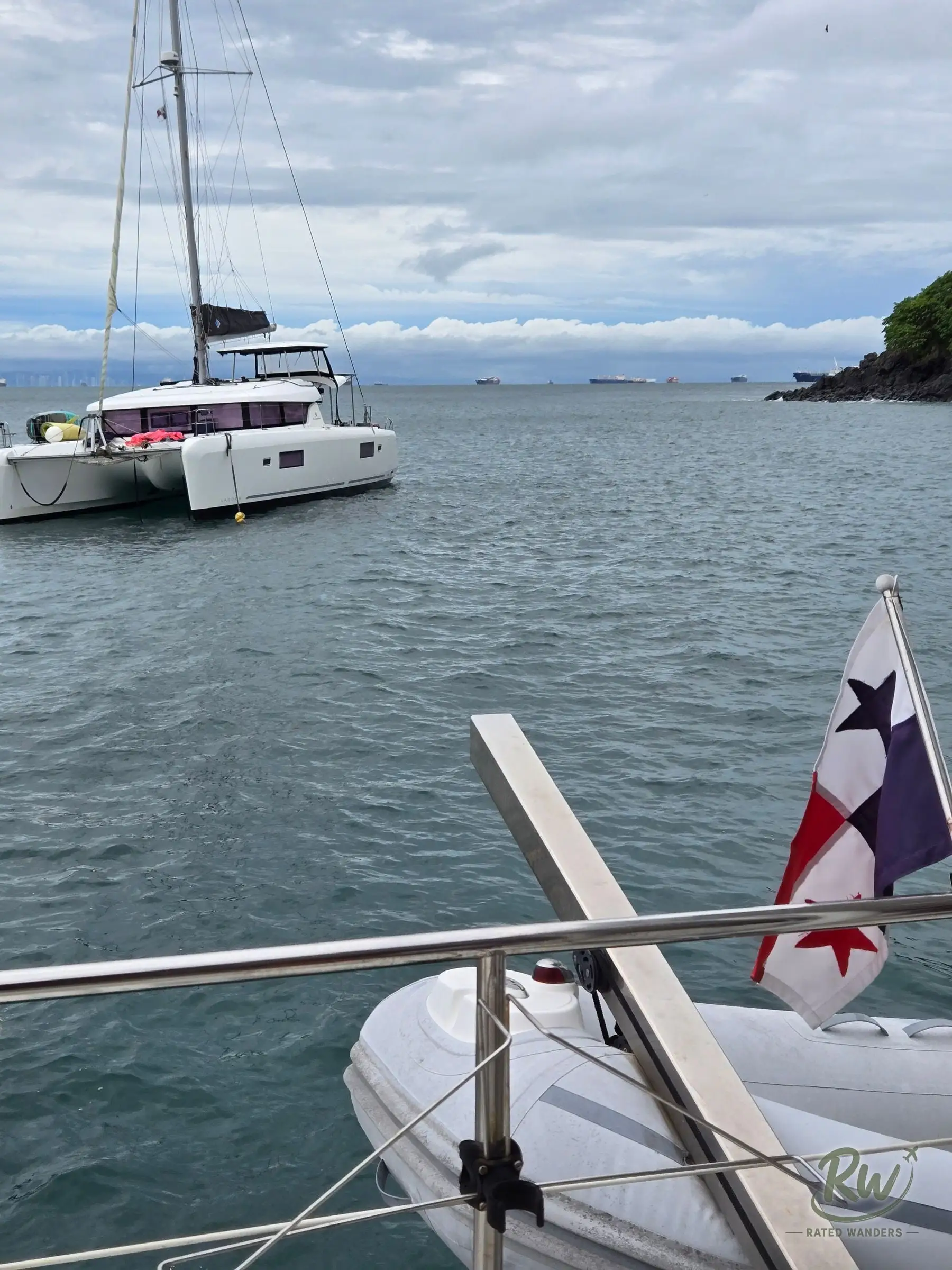 A white catamaran moored off Taboga with cargo ships on the horizon, a Panamanian flag on the rail in the foreground
