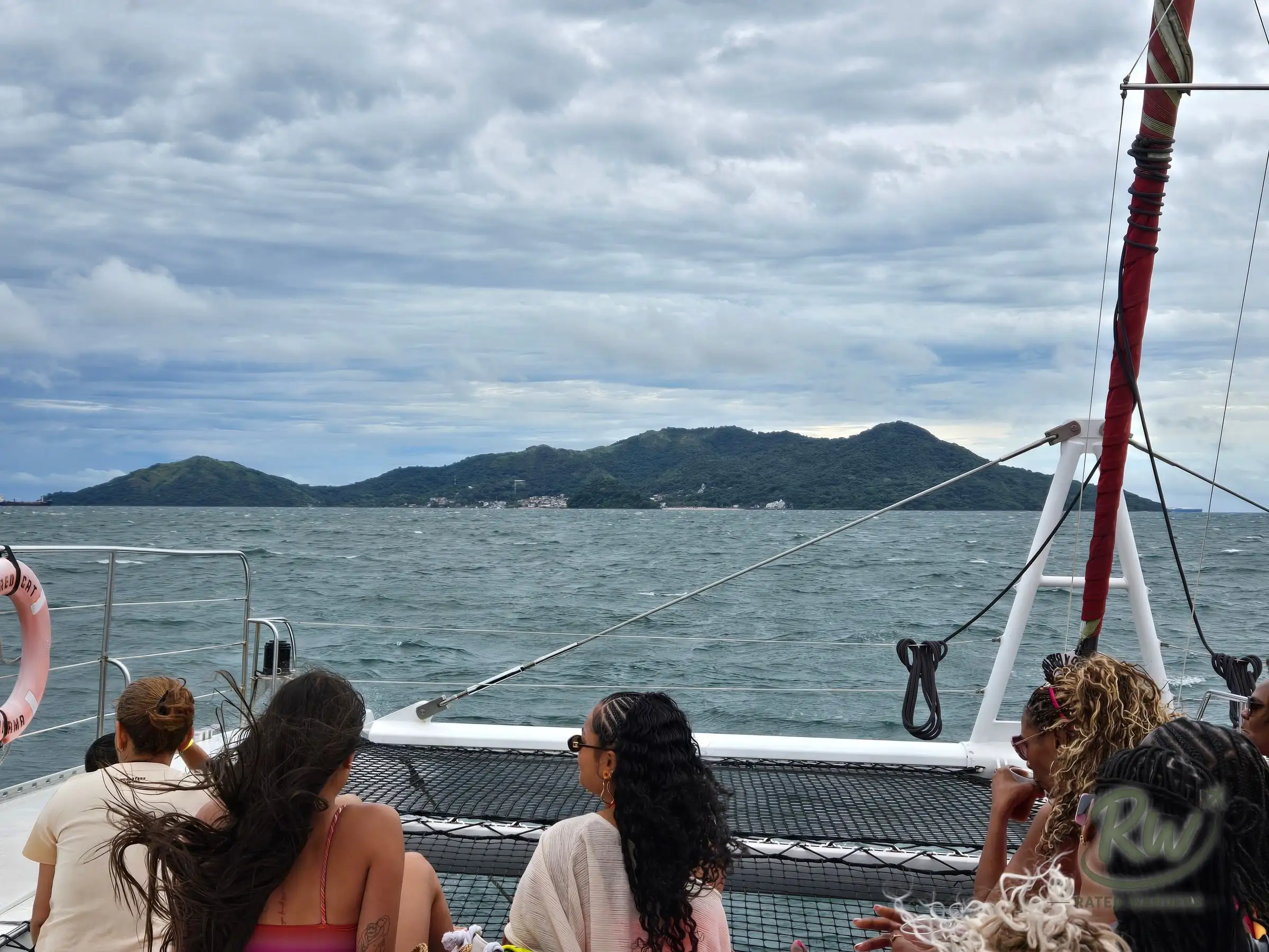 Passengers on a catamaran’s trampoline nets watching Taboga Island’s green hills come into view across choppy water